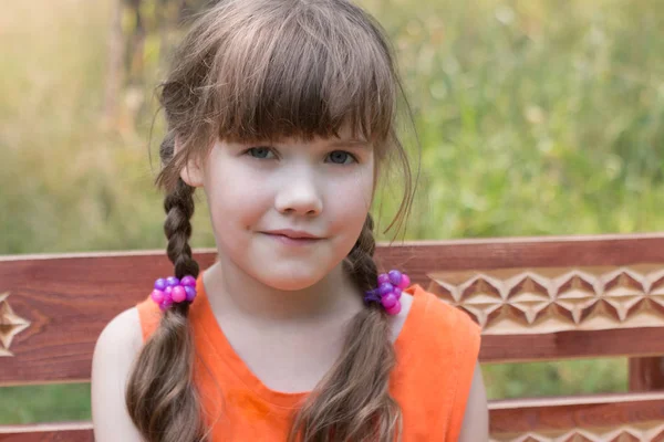 Happy pretty little girl sits on wooden beanch at summer day, sh — Stock Photo, Image