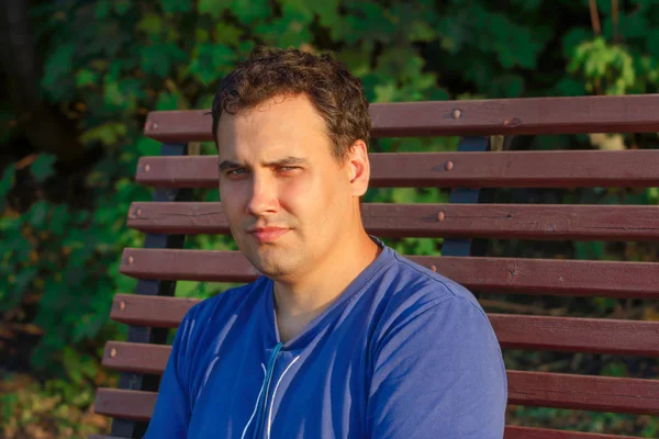 Genç adam bri altında bankta oturmuş sıcak bahar günü