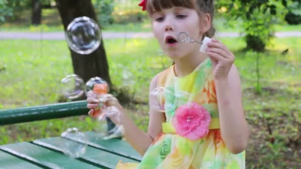 Niña sopla burbujas en el parque verde en el día de verano — Vídeo de stock