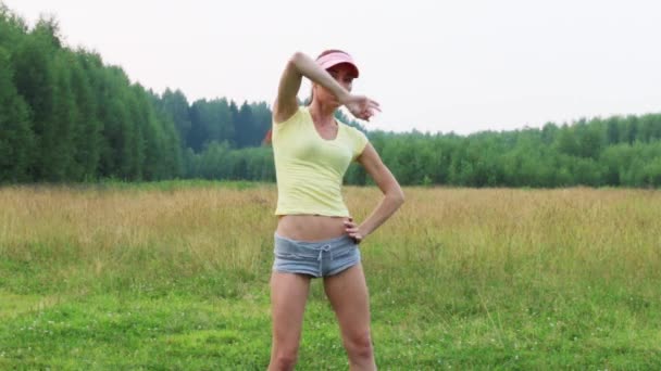 Girl in shorts and cap dances on green meadow at summer evening — Stock Video