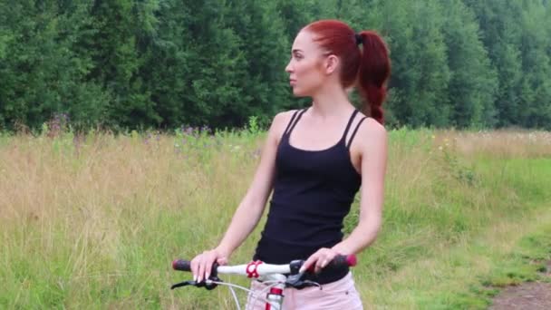 Mooie jonge vrouw staat met fiets en kijkt rond buiten zomer — Stockvideo