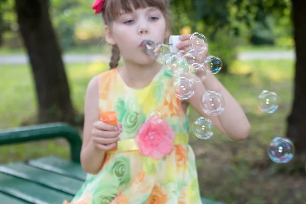 Belle petite fille en robe de couleur qui prend beaucoup de bulles de savon — Photo