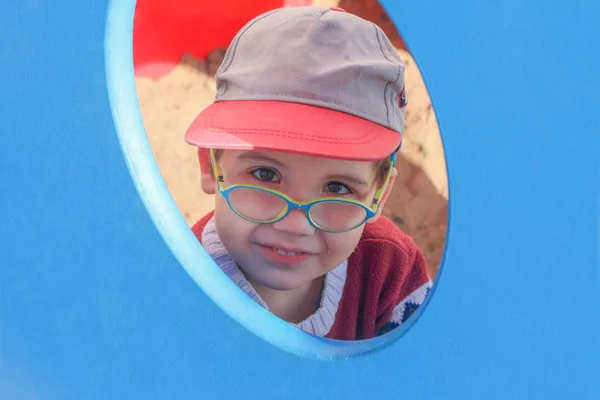 Menino de óculos e chapéu olha pela janela — Fotografia de Stock