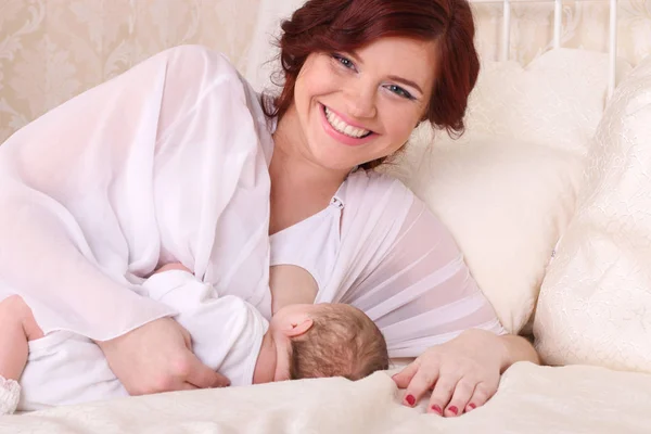 Young mother breastfeeds her baby, holding him in her arms and s — Stock Photo, Image