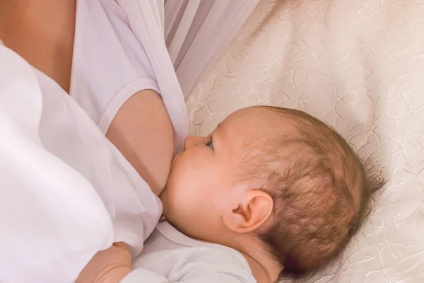Det lilla barnet suger hans mammas bröst på en säng — Stockfoto