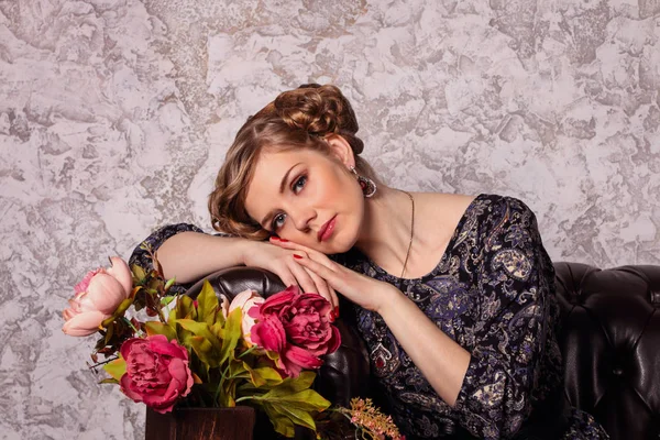 Pretty young woman with hairdo and makeup poses on sofa — Stock Photo, Image