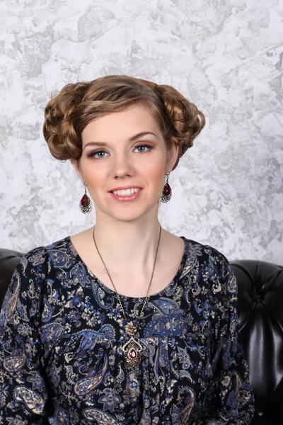 Hübsche junge Frau mit Frisur und im Kleid lächelt auf dem Sofa — Stockfoto