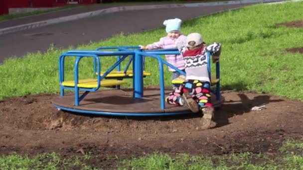 Zwei glückliche Kinder spielen bei sonnigem Wetter auf Kreisverkehr — Stockvideo