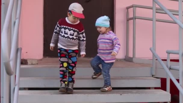 Двое симпатичных маленьких детей играют на лестнице подъезда жилого дома — стоковое видео