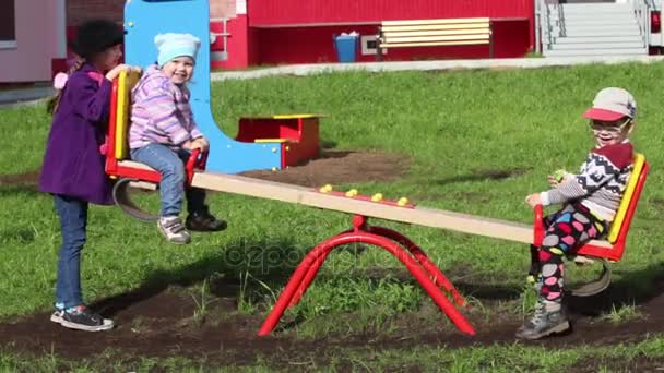 Τρία ευτυχισμένα παιδιά παίζουν στην τραμπάλα στην ηλιόλουστη ημέρα άνοιξη — Αρχείο Βίντεο