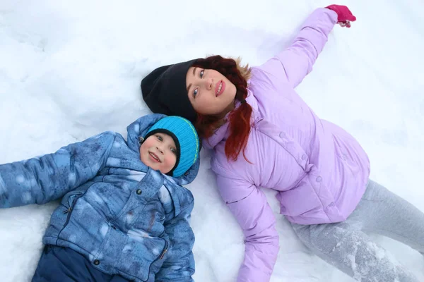Mulher feliz e seu filho mentem na neve branca no dia de inverno — Fotografia de Stock