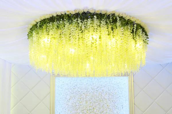 Yellow flowers hanging from ceiling, wall with white artificial