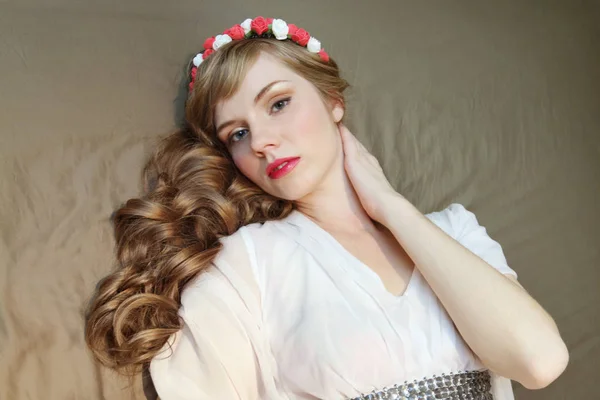 Chica en rosas corona y vestido con pelo rizado se encuentra en la cama y l — Foto de Stock