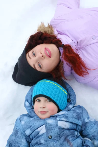 Mulher feliz e seu filho jazem na neve branca no dia de inverno — Fotografia de Stock