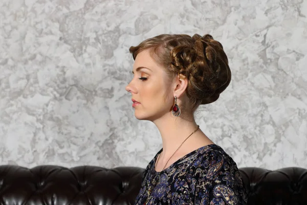 Young woman with hairdo and closed eyes poses on sofa in studio — Stock Photo, Image