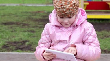 Sıcak elbiseleri kız gülümser ve tablet ile sahada oynuyor