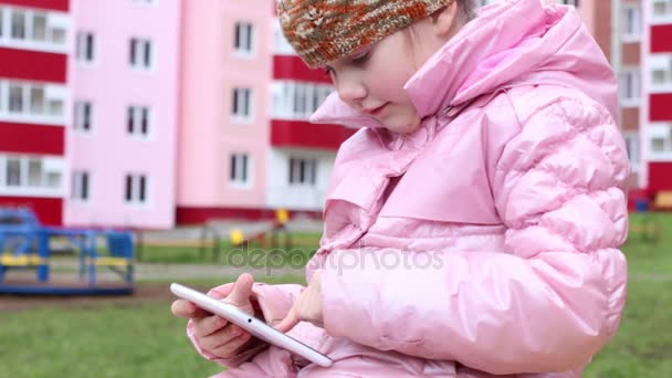 Flicka i varma kläder spelar med tablett på lekplats, närbild — Stockvideo