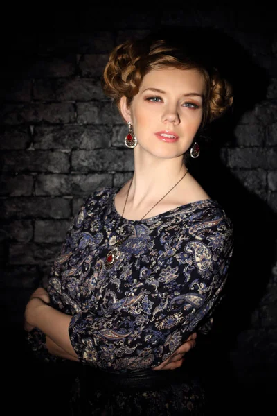 Beautiful young woman with hairdo and jewelry poses in dark — Stock Photo, Image