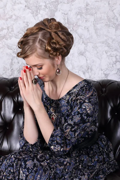 Young woman with hairdo prays with closing eyes on sofa in room — Stock Photo, Image