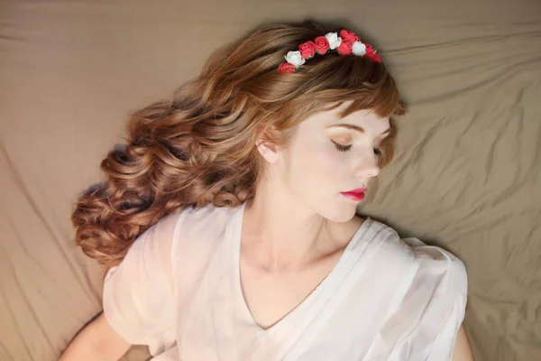 Träumendes Mädchen in Rosenkranz und Kleid mit lockigem Haar lügt — Stockfoto