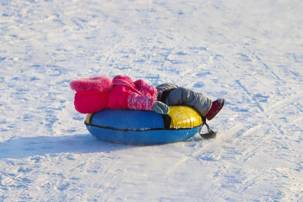 Liten flicka ligger på snowtube från hill på solig vinterdag — Stockfoto