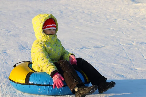 Menina senta-se no tubo de neve e olha para o inverno ensolarado e gelado — Fotografia de Stock