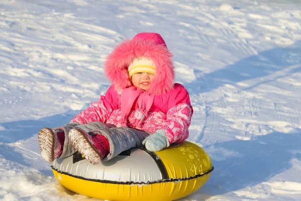 Lilla flickan glider på snowtube ner från backen på solig vinter — Stockfoto