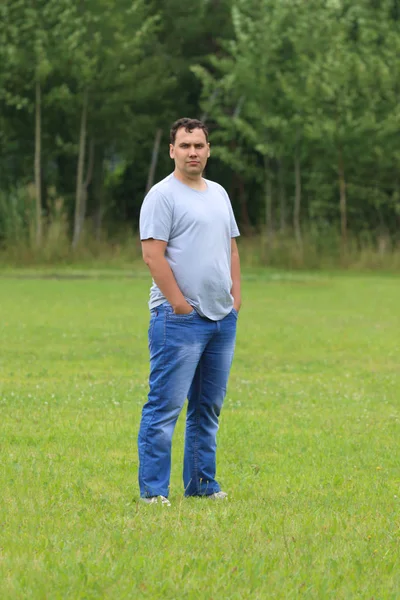 Jonge man in spijkerbroek staat op groen gras op weide op zomerdag — Stockfoto