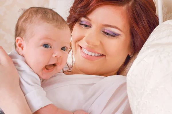 Beautiful young mom that keeps her child in her arms, lying on t — Stock Photo, Image