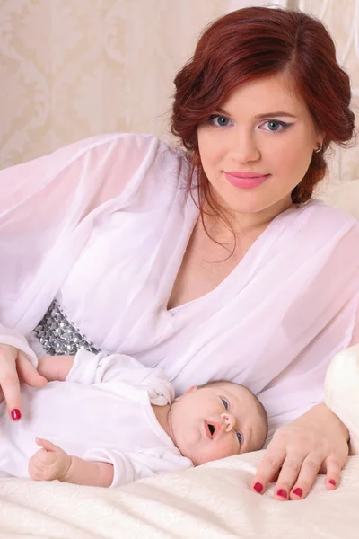 Una joven madre con un vestido blanco de seda acostada en la cama junto a él — Foto de Stock
