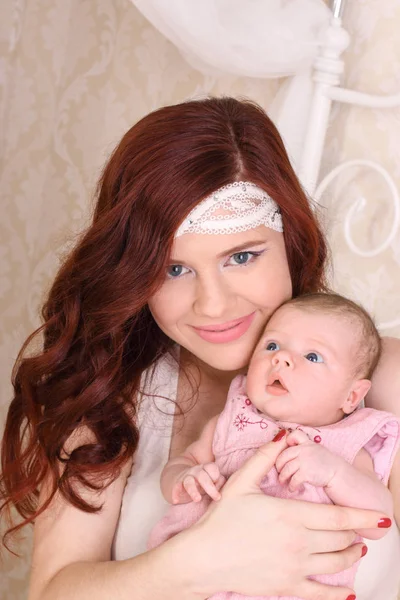 Happy young mother in a white silk dress, holds her baby in her — Stock Photo, Image