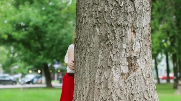 Petite fille se cachant et regardant du grand arbre dans le parc d'été — Video