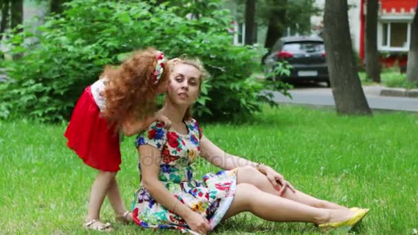 Little girl kisses her mother on lawn in summer park — Stock Video