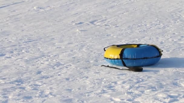 O tubo de neve amarelo e azul está na neve branca no dia ensolarado do inverno — Vídeo de Stock