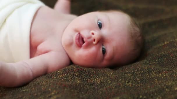 Bebê bonito é enrolado em pano branco deitado na cama e mãos em movimento — Vídeo de Stock