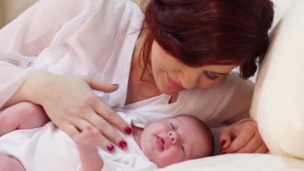 Jonge moeder lijnen haar kleine schattige baby in witte bed in de slaapkamer — Stockvideo