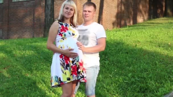 Беременная женщина и счастливый мужчина позируют в летнем зеленом парке — стоковое видео