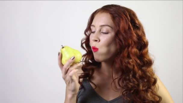 Красивая молодая женщина кусает свежую грушу в белой студии, видео со звуком — стоковое видео