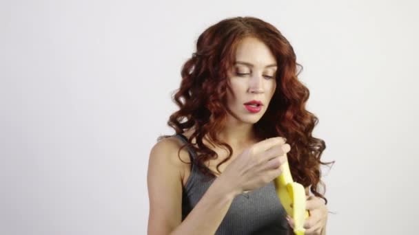 Jovem mulher descasca e come banana em estúdio branco, vídeo com som — Vídeo de Stock