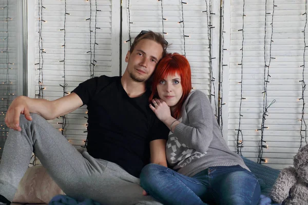 Heureuse fille aux cheveux roux et jeune homme assis ensemble dans un studio blanc — Photo