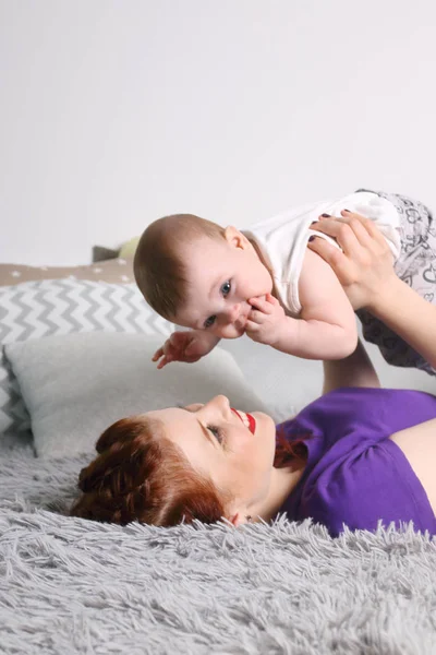 Happy mother plays with her little baby on bed with pillows in r — Stock Photo, Image