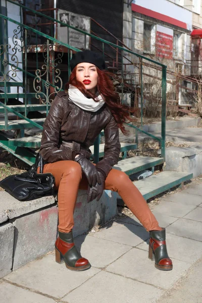 Girl in leather jacket and beret sits near stairs outdoor at sun — Stock Photo, Image