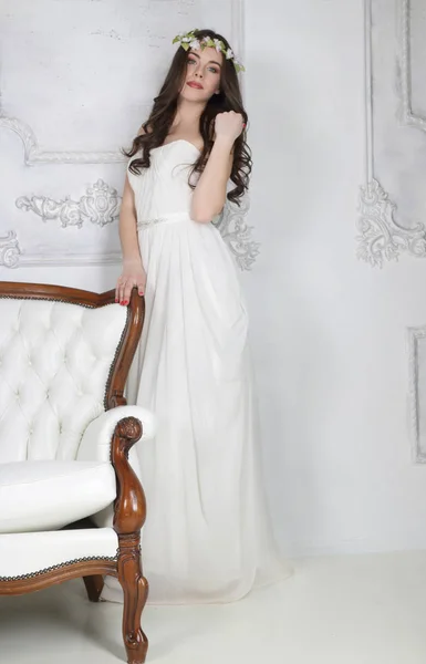 Joven morena linda en corona y en vestido blanco posa cerca de couc — Foto de Stock