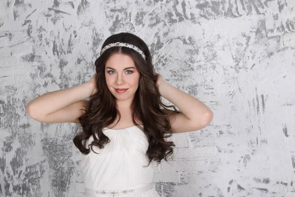 Pretty young brunette in diadem poses near brick wall in white s — Stock Photo, Image