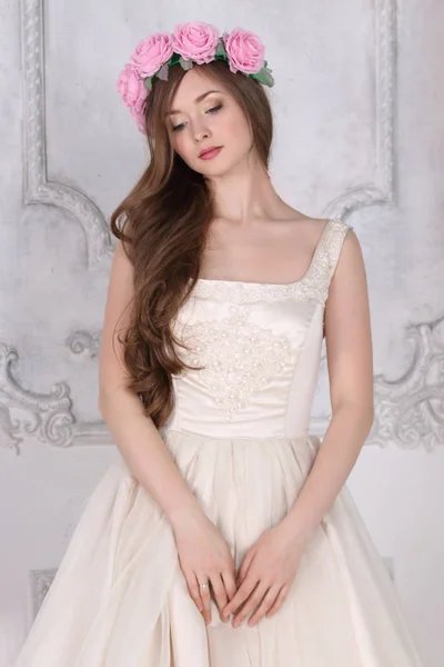 Красивая женщина в розах венок и платье позирует в белой студии — стоковое фото