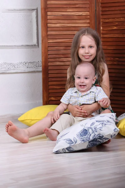 Happy little girl with brother sit on floor among pillows near w — Stock Photo, Image