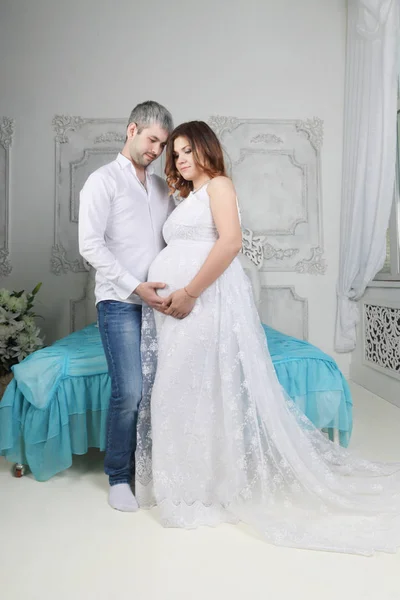 Pregnant woman in long dress and man stand together in bedroom — Stock Photo, Image