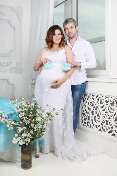 Mujer embarazada en vestido y hombre con bootees de bebé en el dormitorio — Foto de Stock