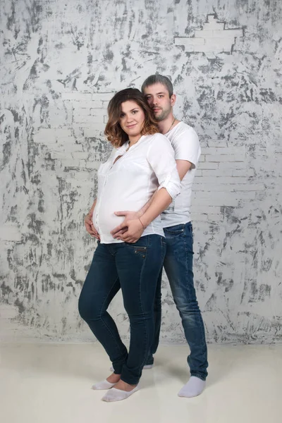 Young pretty pregnant woman and man in jeans poses in white stud — Stock Photo, Image