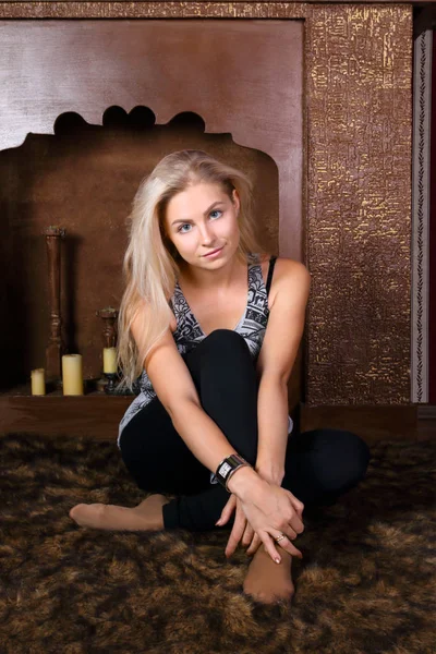 Pretty young woman sits on fur carpet in studio with decorative — Stock Photo, Image